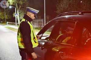 Zdjęcie kolorowe. Zdjęcie zrobione nocą. Policjanci kontrolują stan trzeźwosci kierujących
