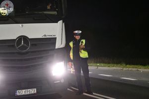 Zdjęcie kolorowe. Zdjęcie zrobione nocą. Policjanci kontrolują stan trzeźwosci kierujących