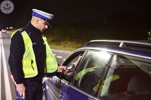 Zdjęcie kolorowe. Zdjęcie zrobione nocą. Policjanci kontrolują stan trzeźwosci kierujących