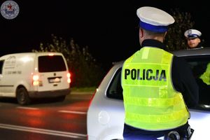 Zdjęcie kolorowe. Zdjęcie zrobione nocą. Policjanci kontrolują stan trzeźwosci kierujących