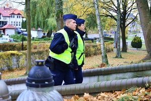 Zdjęcie kolorowe. Policjanci idą po schodach na cmentrzu