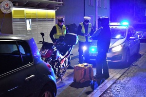 Zdjęcie kolorowe. Policjanci po zmroku kontrolują kierującego motorowerem.