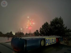 Zdjęcie kolorowe. Noc. Na niebie rozbłyskujące się fajerwerki. Na pierwszym planie galeryjka na dachu policyjnego radiowozu.