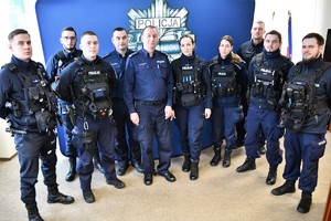Zdjęcie kolorowe. Komendant na granatowej ściance stoi w towarzystwie młodych policjantów