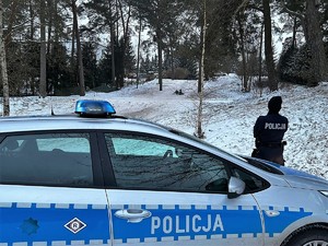 Zdjęcie kolorowe. Na pierwszym planie radiowóz za nim policjantka, które obserwuje zjeżdżające na sankach dzieci