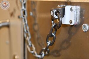 Zdjęcie kolorowe. Zbliżenie na zabezpieczenie zewnętrzne metalowych drzwi na tzw. łańcuch