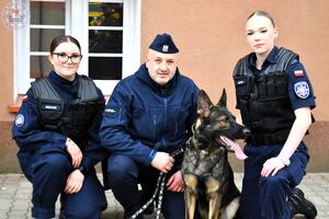 Zdjęcie kolorowe. Wspólne zdjęcie dwóch uczennic i przewodnika z psem służbowym