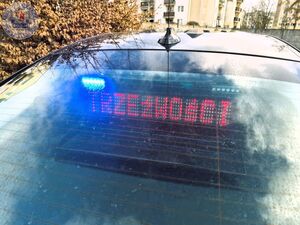 Zdjęcie kolorowe. Tylna szybka samochodu a za nią widoczna kamera i ekran z wyświetlonym napisem trzeźwość