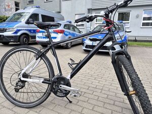 Zdjęcie kolorowe. Rower na tle zaparkowanych pojazdów w tle budynek komendy policji