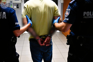 Zdjęcie kolorowe. Policjanci prowadzą osobę zatrzymaną