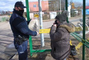 Dzielnicowy wręcza kobiecie torbę na przystanku autobusowym