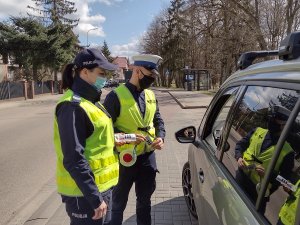 Zdjęcie kolorowe. Dwaj umundurowani policjanci rozmawiają z kierowca siedzącym w samochodzie.